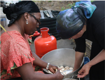Two members of the Chickpea Sisters cooking over a large pot.